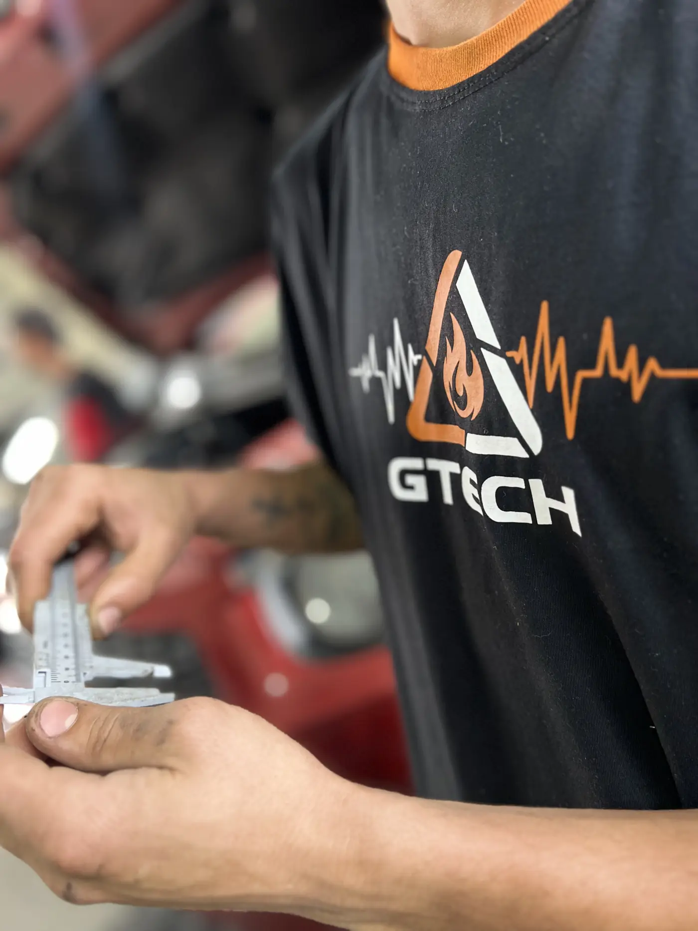 Mecânico com a camiseta da GTech medindo uma peça com paquímetro
