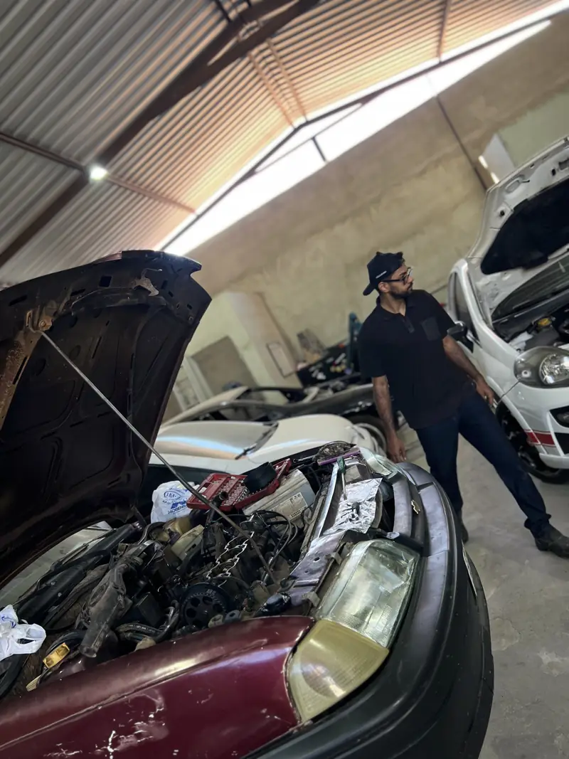 Mecânico ao lado de carro com o capô aberto na oficina